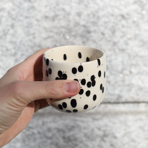 Tasse à café latte Black Dots en grès avec émail noir et blanc tenue à la main.