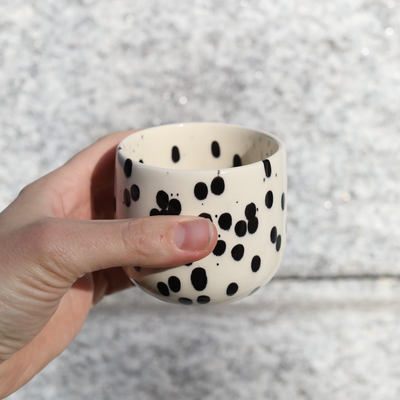 Tasse à café latte Black Dots en grès avec émail noir et blanc tenue à la main.