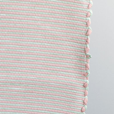 Close-up d'un tapis de salle de bain bicolore rayé rose et vert menthe fabriqué à partir de chutes de coton