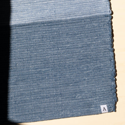 Close-up du bas d'un petit tapis bleu foncé avec le logo A d'Atelier Agave