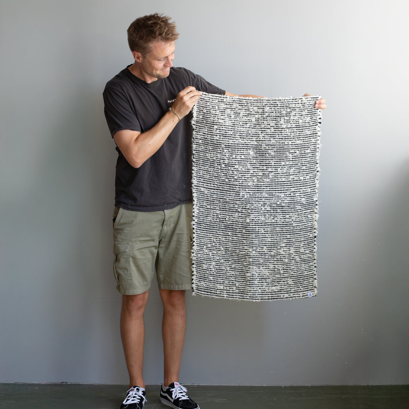 Petit tapis de 60x90cm tenu par une personne, en tissu éponge blanc avec des rayures noires, tissé à la main au Portugal.