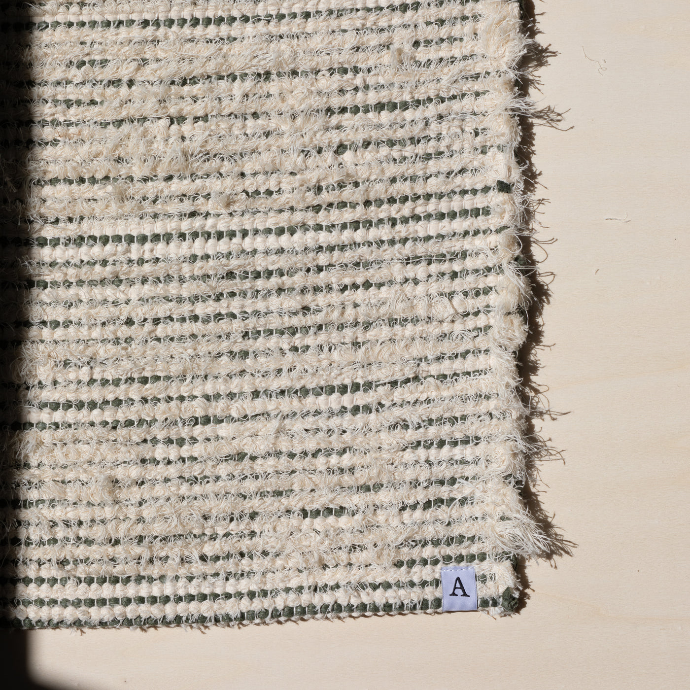 Closeup d'un petit tapis 60x80cm rayé avec du coton vert olive et du tissu éponge blanc dans la lumière du soleil