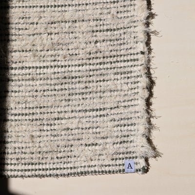 Closeup d'un petit tapis 60x80cm rayé avec du coton vert olive et du tissu éponge blanc dans la lumière du soleil