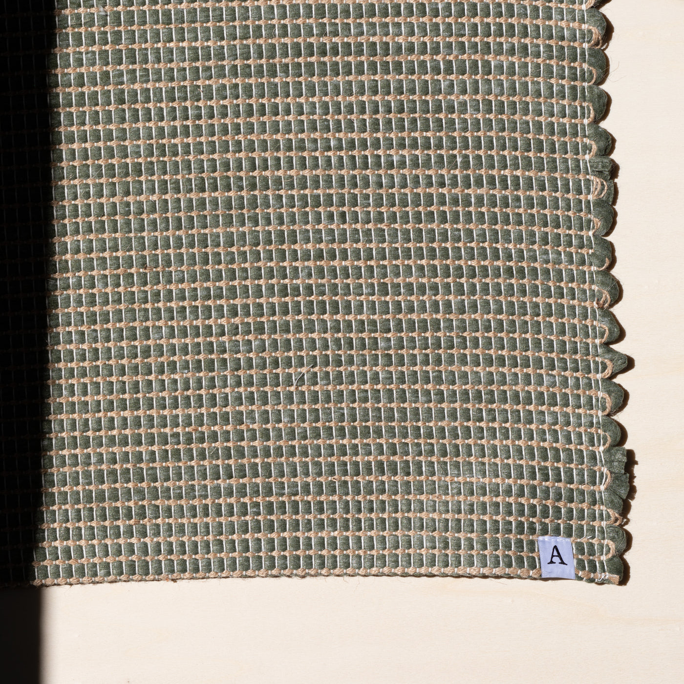 Close-up d'un petit tapis 60x90cm en vert avec du jute entrelacé tissé à la main en coton upcycling au Portugal