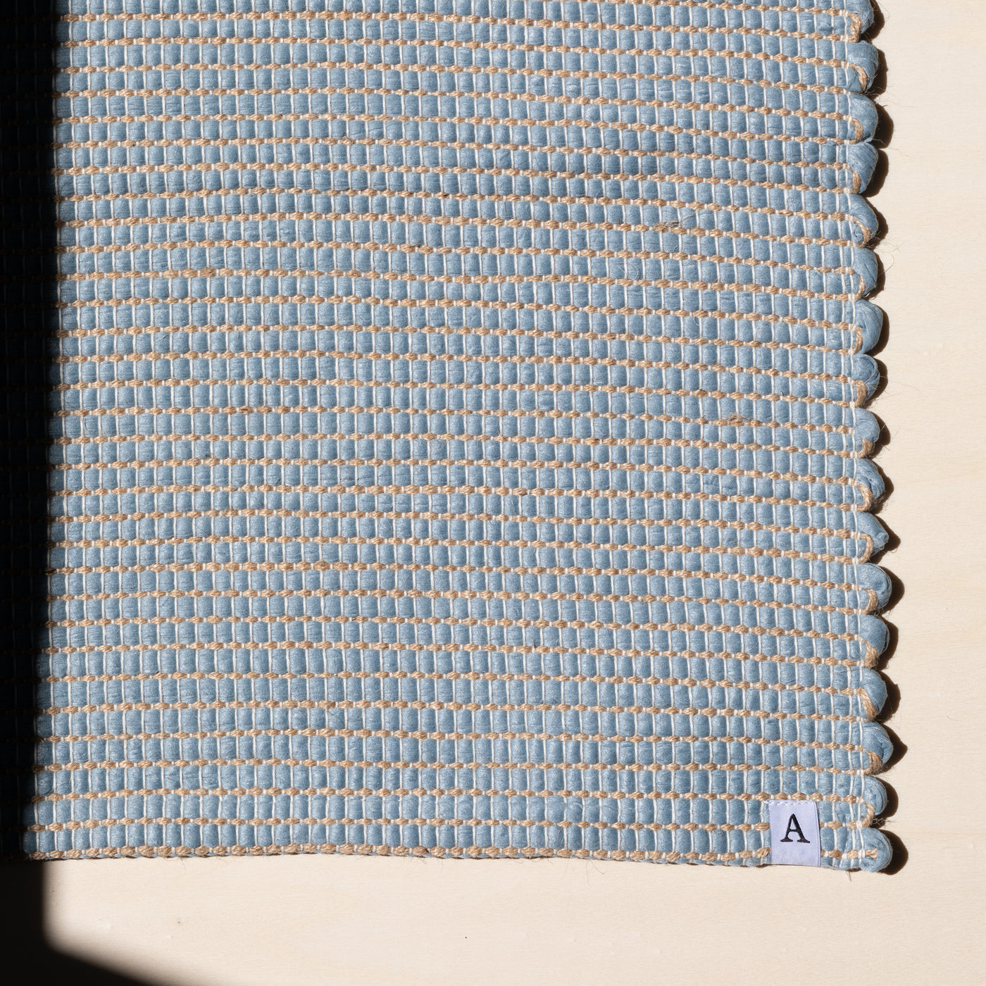 Close-up d'un petit tapis 60x90cm en bleu clair avec du jute entrelacé tissé à la main en coton upcycling au Portugal