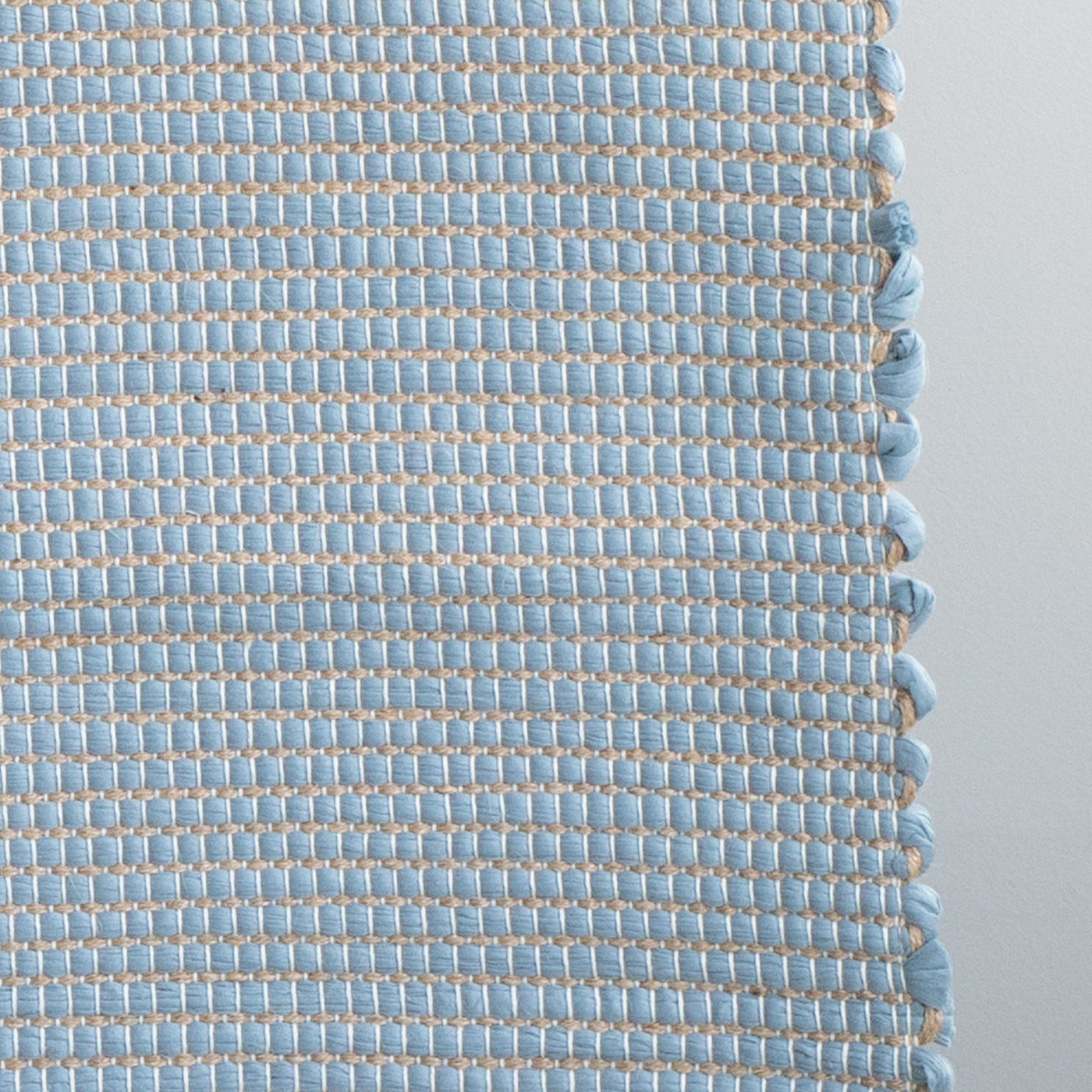 Closeup d'un tapis de salle de bain bleu clair rayé de jute, fabriqué à partir de chutes de laine provenant de l'industrie textile et tissé à la main au Portugal.