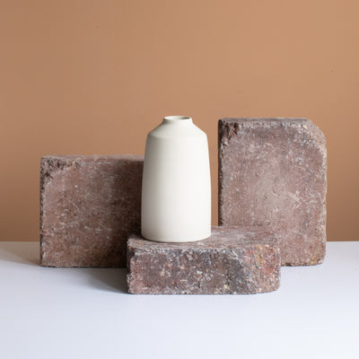Un vase de fleurs beige repose sur une brique brun rouille