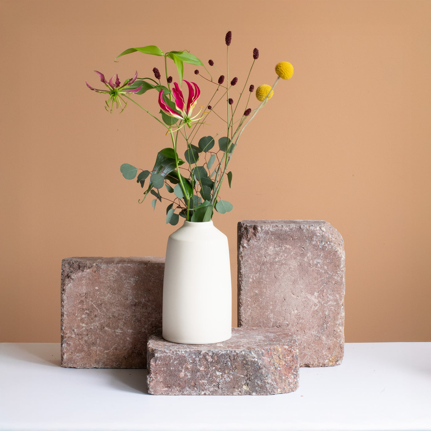 Vase couleur crème avec un strass floral rouge et jaune posé sur une brique brun rouille