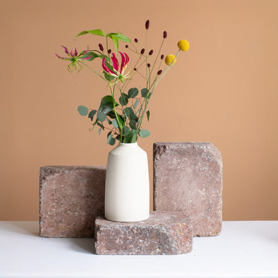 Vase couleur crème avec un strass floral rouge et jaune posé sur une brique brun rouille