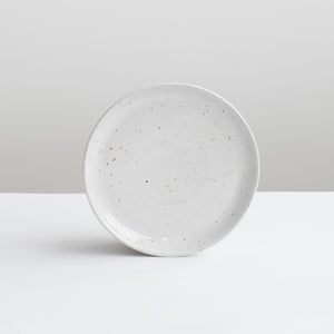 Petite assiette blanche à hors-d'œuvre en blanc avec de fines mouchetures dorées sur fond gris