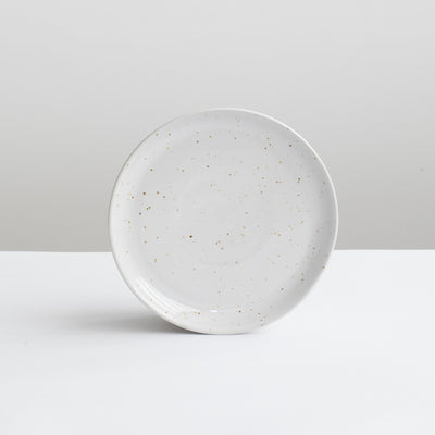 Petite assiette blanche à hors-d'œuvre en blanc avec de fines mouchetures dorées sur fond gris