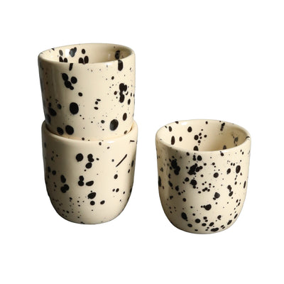 Deux tasses à expresso empilées et une tasse beige à pois noirs sur fond blanc.