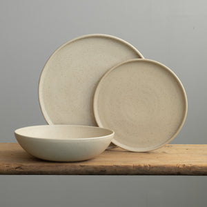 Set de vaisselle en speckled beige avec une grande assiette, une petite assiette posée sur le dessus et une assiette creuse à pâtes devant. 