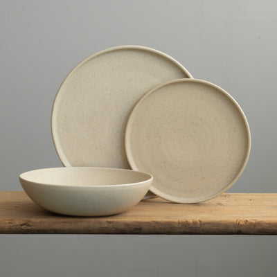Set de vaisselle en speckled beige avec une grande assiette, une petite assiette posée sur le dessus et une assiette creuse à pâtes devant. 