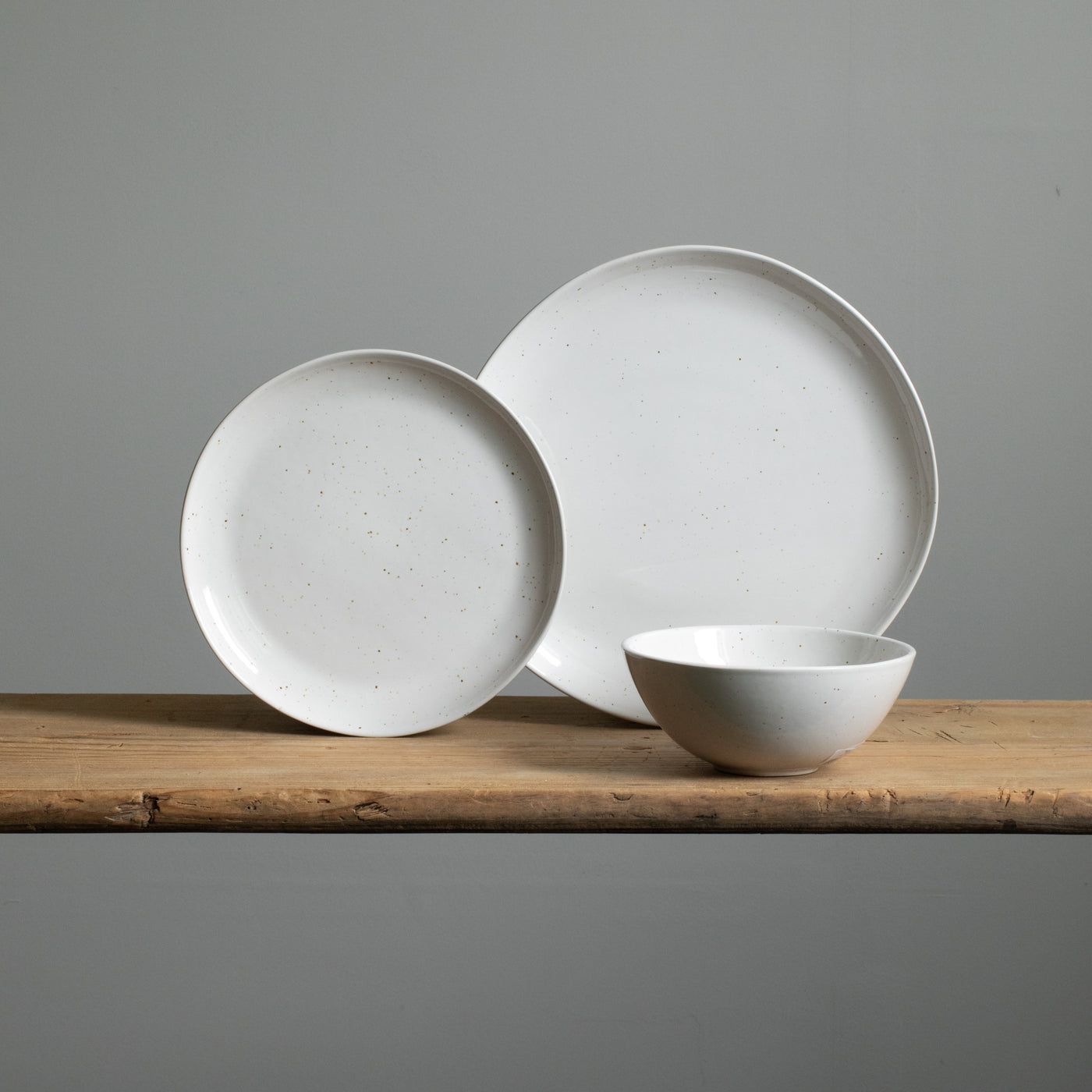 Une petite assiette en grès dressée à côté d'une assiette de plat principal et devant un bowl de muesli blanc