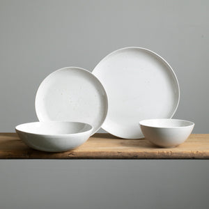 Quatre types d'assiettes différents sur une table en bois. Devant, une assiette de pâtes et un bol de muesli en émail blanc avec de fines taches dorées.
