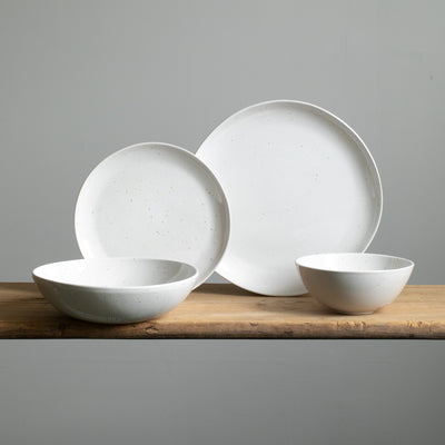 Quatre types d'assiettes différents sur une table en bois. Devant, une assiette de pâtes et un bol de muesli en émail blanc avec de fines taches dorées.