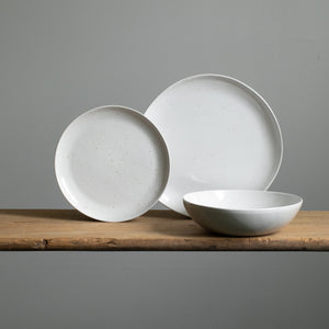 On voit une grande assiette de plat principal et une petite assiette d'entrée posées devant une assiette creuse de pâtes avec un glaçage blanc.