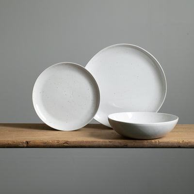 On voit une grande assiette de plat principal et une petite assiette d'entrée posées devant une assiette creuse de pâtes avec un glaçage blanc.