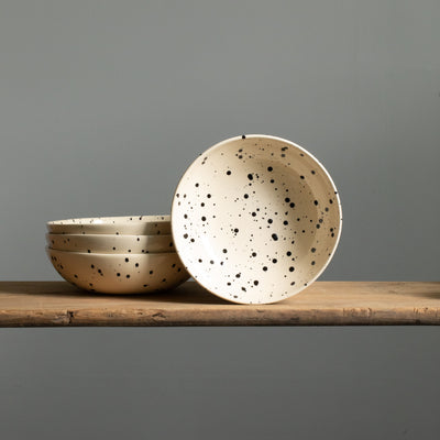 Assiette principale beige avec des touches de noir à l'avant et trois assiettes de pâtes empilées
