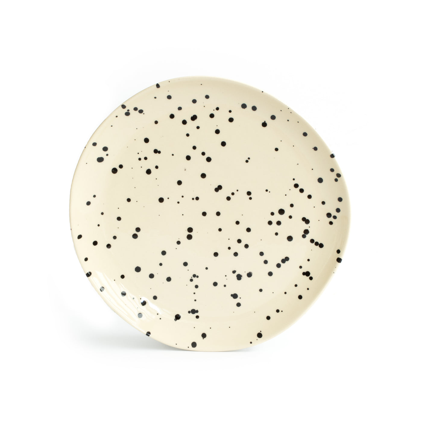 Une grande assiette beige avec des éclaboussures de peinture noire et un arrière-plan blanc.