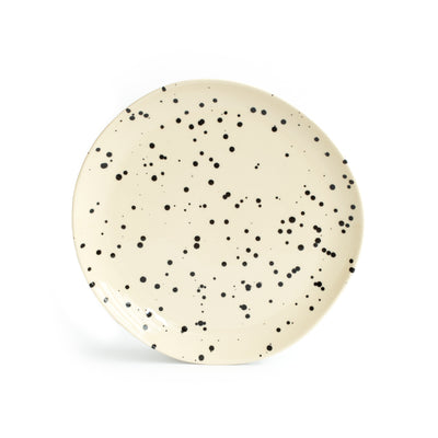Une grande assiette beige avec des éclaboussures de peinture noire et un arrière-plan blanc.