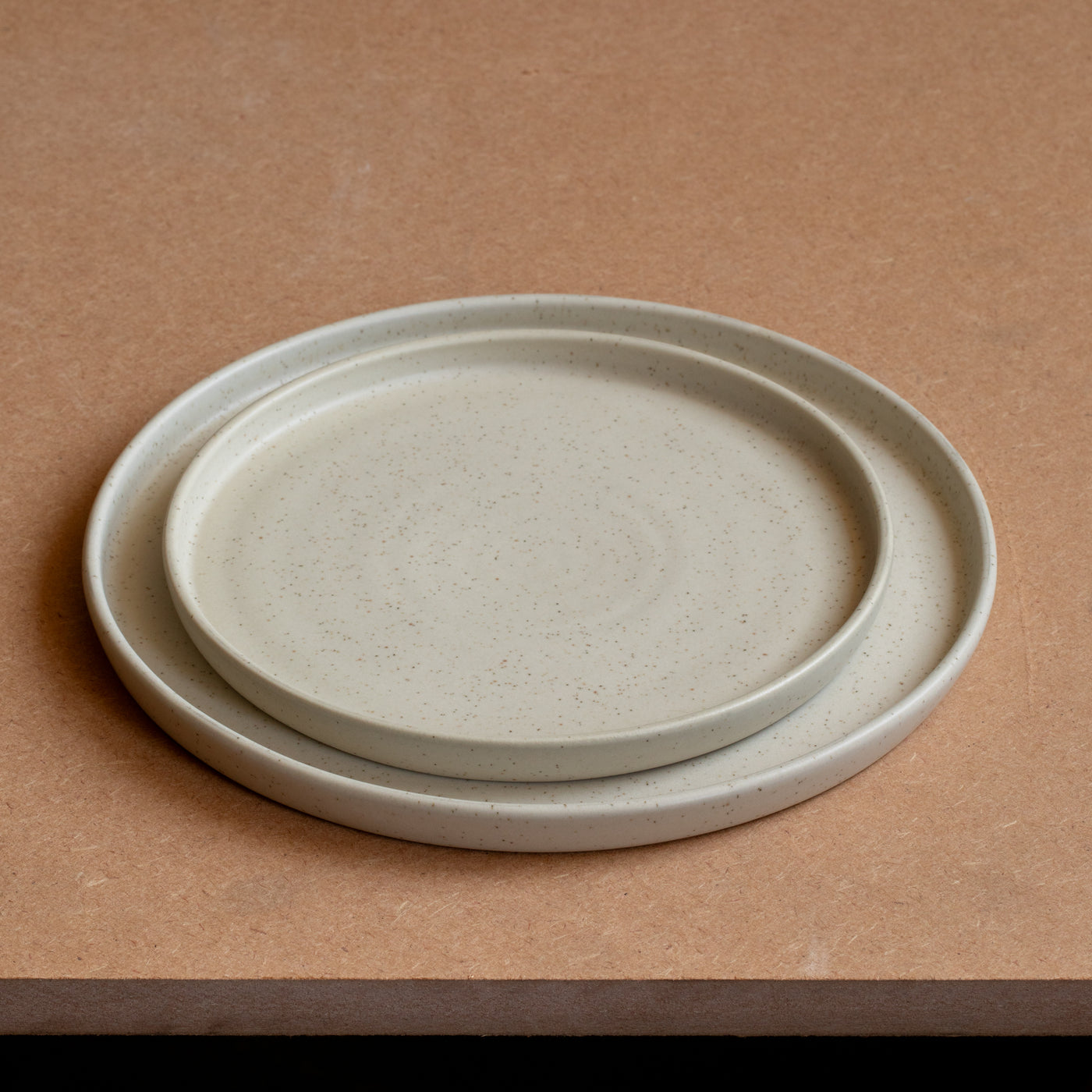 La petite assiette repose dans la grande assiette Les deux ont un bord droit et sont beige mat