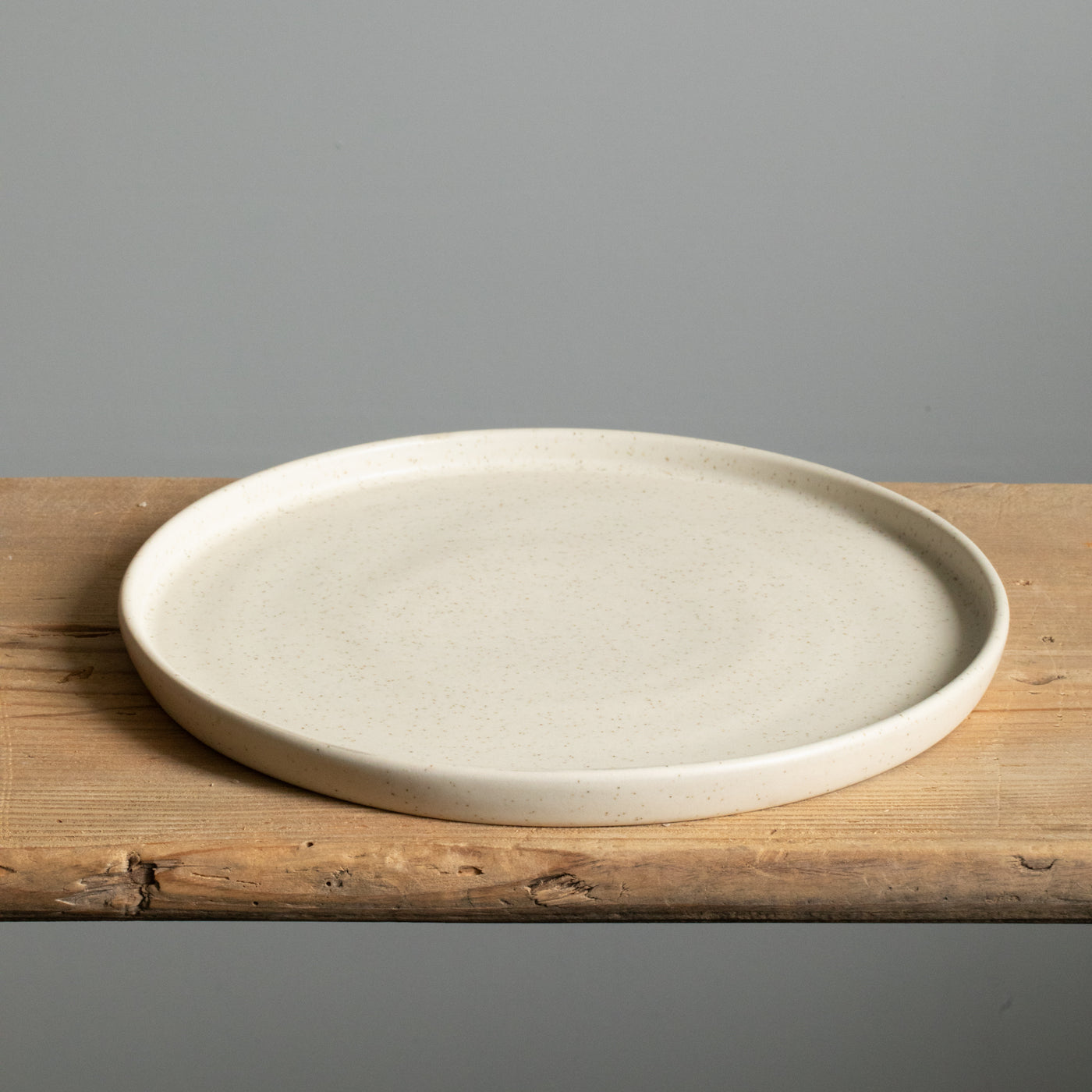 Grande assiette beige mate à bord droit posée sur une planche en bois