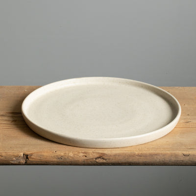 Grande assiette beige mate à bord droit posée sur une planche en bois