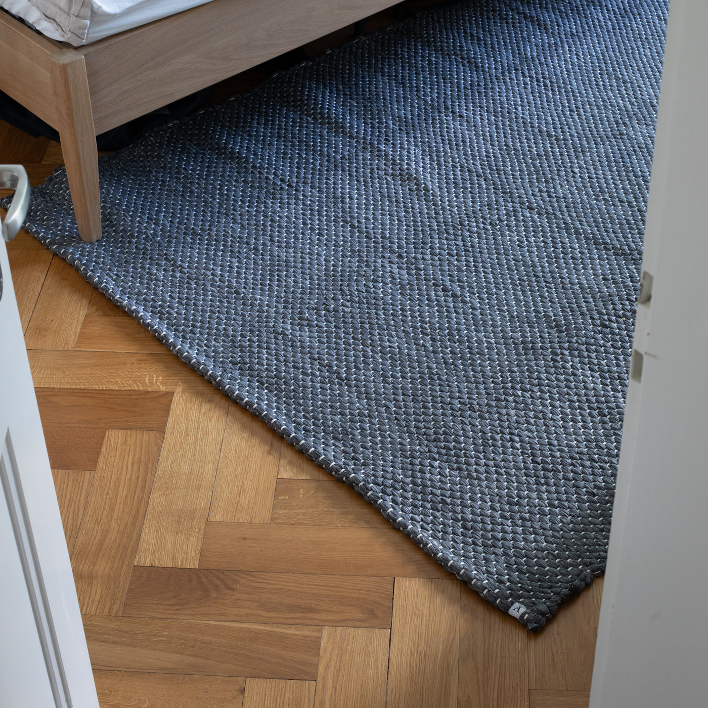 Un grand tapis gris au motif tissé à la main est posé devant un lit 