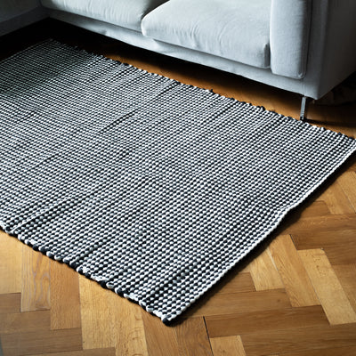 Un grand tapis noir et blanc est posé devant un canapé sur un sol en bois 