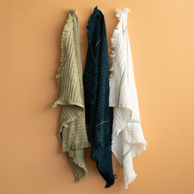Set de serviettes gaufrées en bleu, vert et blanc suspendues devant un mur en terre cuite