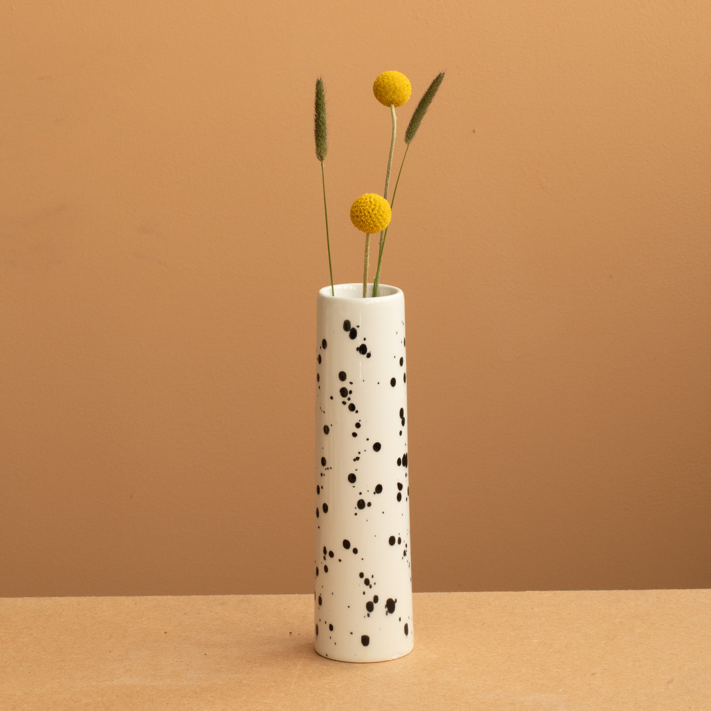 petit vase étroit de couleur beige avec des points noirs avec des fleurs jaunes.