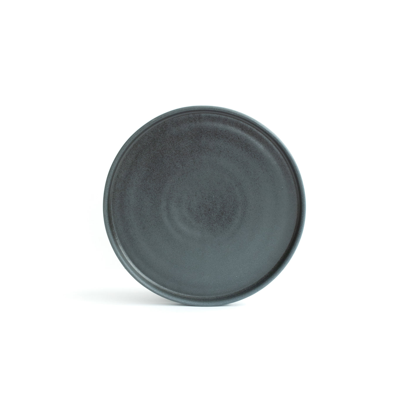Petite assiette noire mate avec bord incliné posée et dégagée