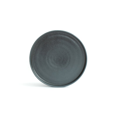 Petite assiette noire mate avec bord incliné posée et dégagée