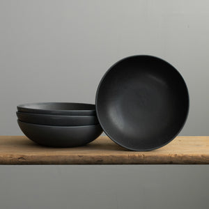 Assiette de pâtes noire mate empilée en grès sur une table en bois