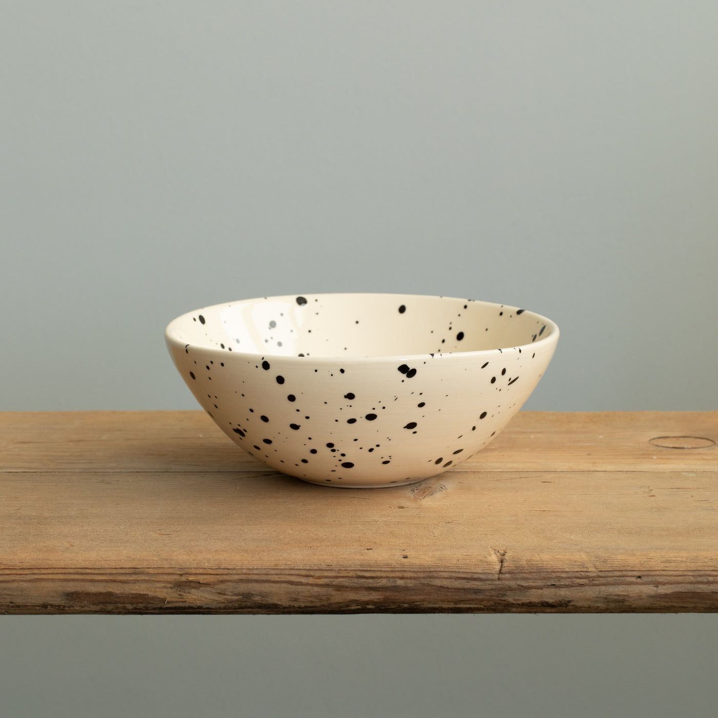 Un petit bol à pois noirs dans le style des Pouilles avec un bord légèrement ouvert vers l'extérieur sur une table en bois.