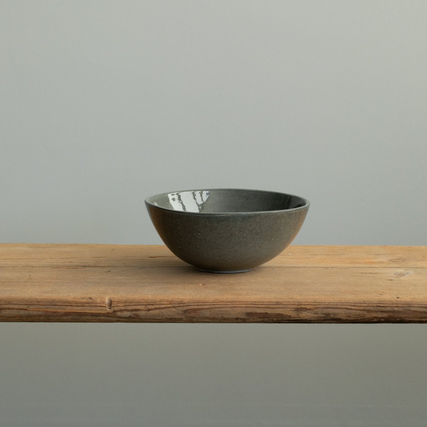 Un bol à déjeuner gris foncé brillant avec un bord légèrement ouvert vers l'extérieur sur une table en bois