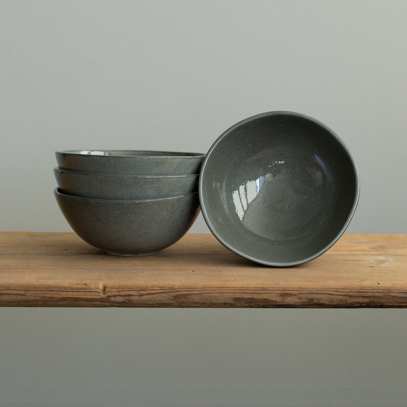 Trois bols à muesli gris foncé empilés et un petit bol posé sur une planche en bois