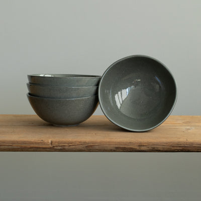 Trois bols à muesli gris foncé empilés et un petit bol posé sur une planche en bois