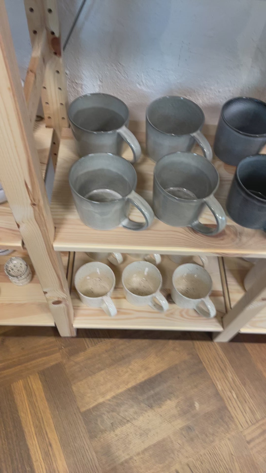 Une grande tasse à thé gris clair est prise sur l'étagère et tournée dans tous les sens afin de bien mettre en valeur la grande surface ronde de l'intérieur ainsi que l'anse généreuse.