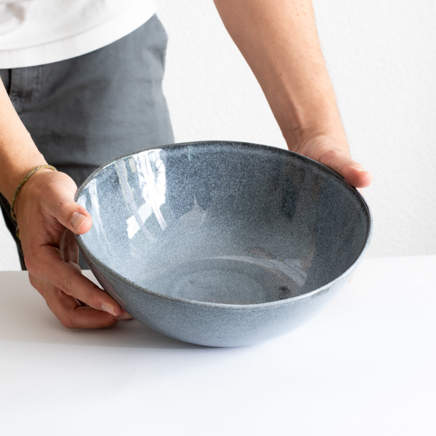 Saladier bleu profond tenu par des mains sur une table blanche 