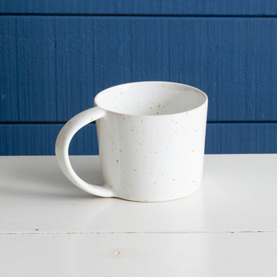 Grande tasse à thé en céramique avec anse en émail réactif blanc avec spots brun doré devant un mur bleu