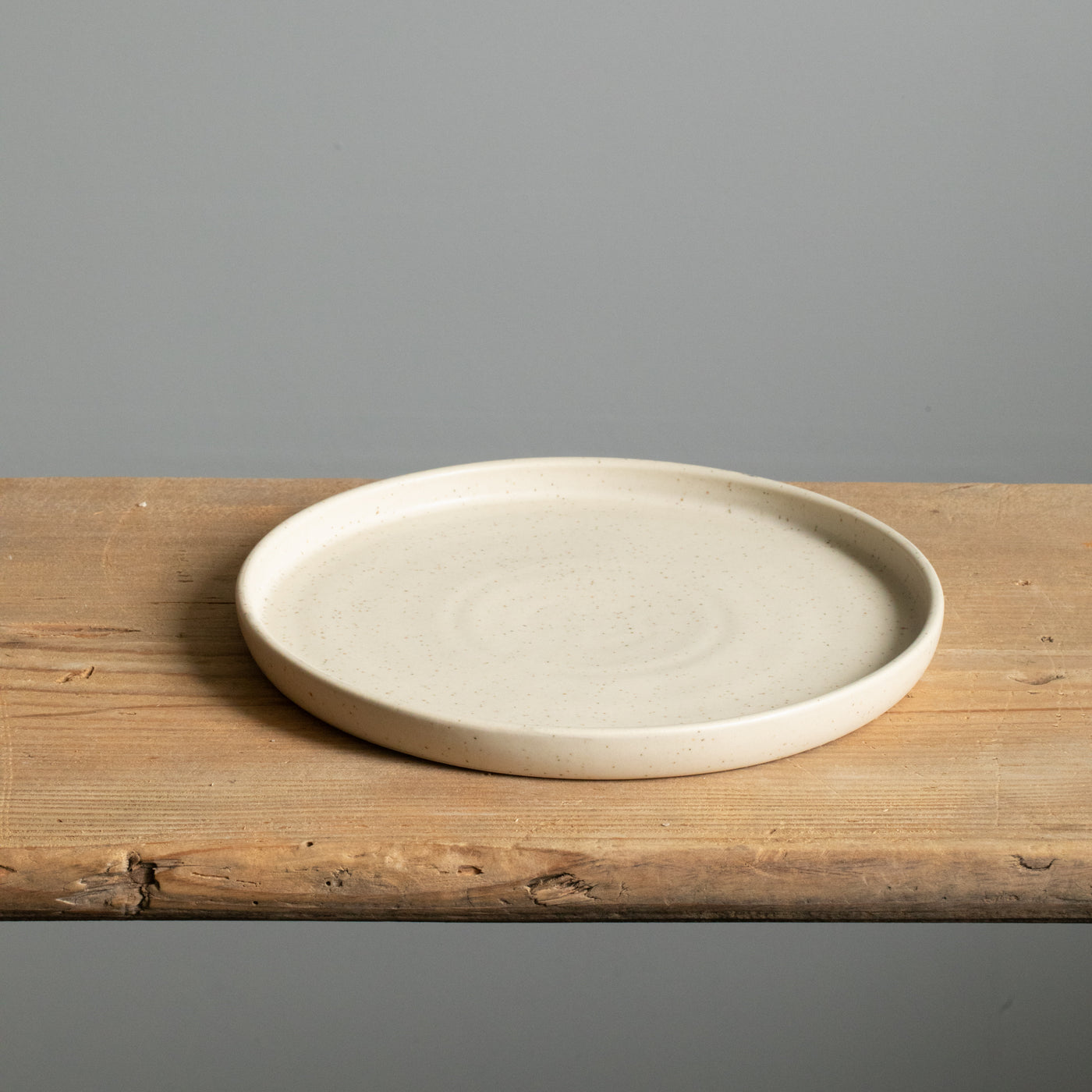 Petite assiette beige à bord droit avec glaçure mate posée sur une planche en bois