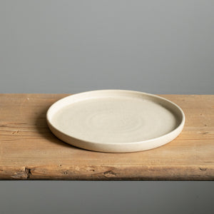 Petite assiette beige à bord droit avec glaçure mate posée sur une planche en bois