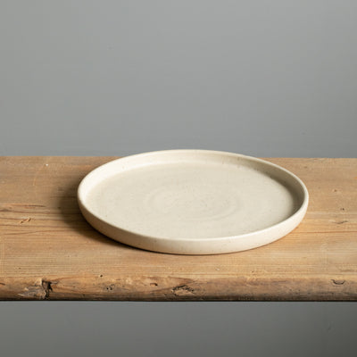 Petite assiette beige à bord droit avec glaçure mate posée sur une planche en bois