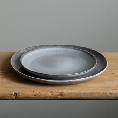 Une grande assiette organique sous une petite assiette à hors-d'œuvre bleue en grès robuste