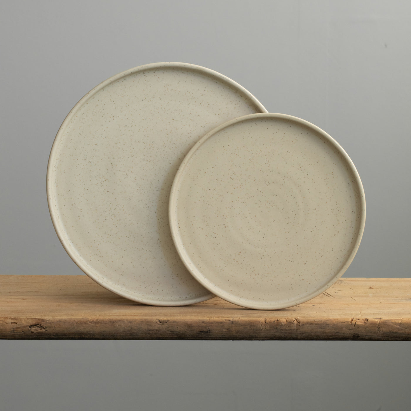Grande et petite assiette à bord droit en émail mat beige posée sur une table en bois