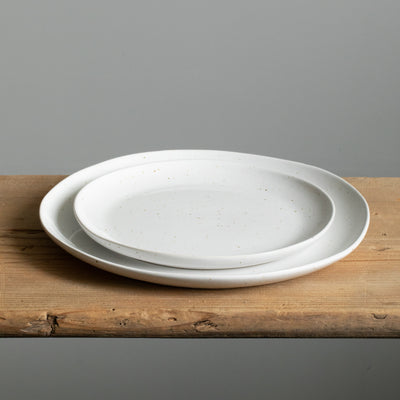 Une petite assiette est posée sur une grande assiette. Les deux ont une forme organique et sont blanches avec des taches brun doré.