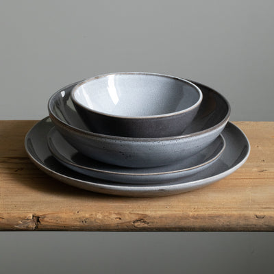 Set complet de vaisselle en grès empilée. Grande assiette, petite assiette, une assiette à pâtes et un bol à céréales en bleu.